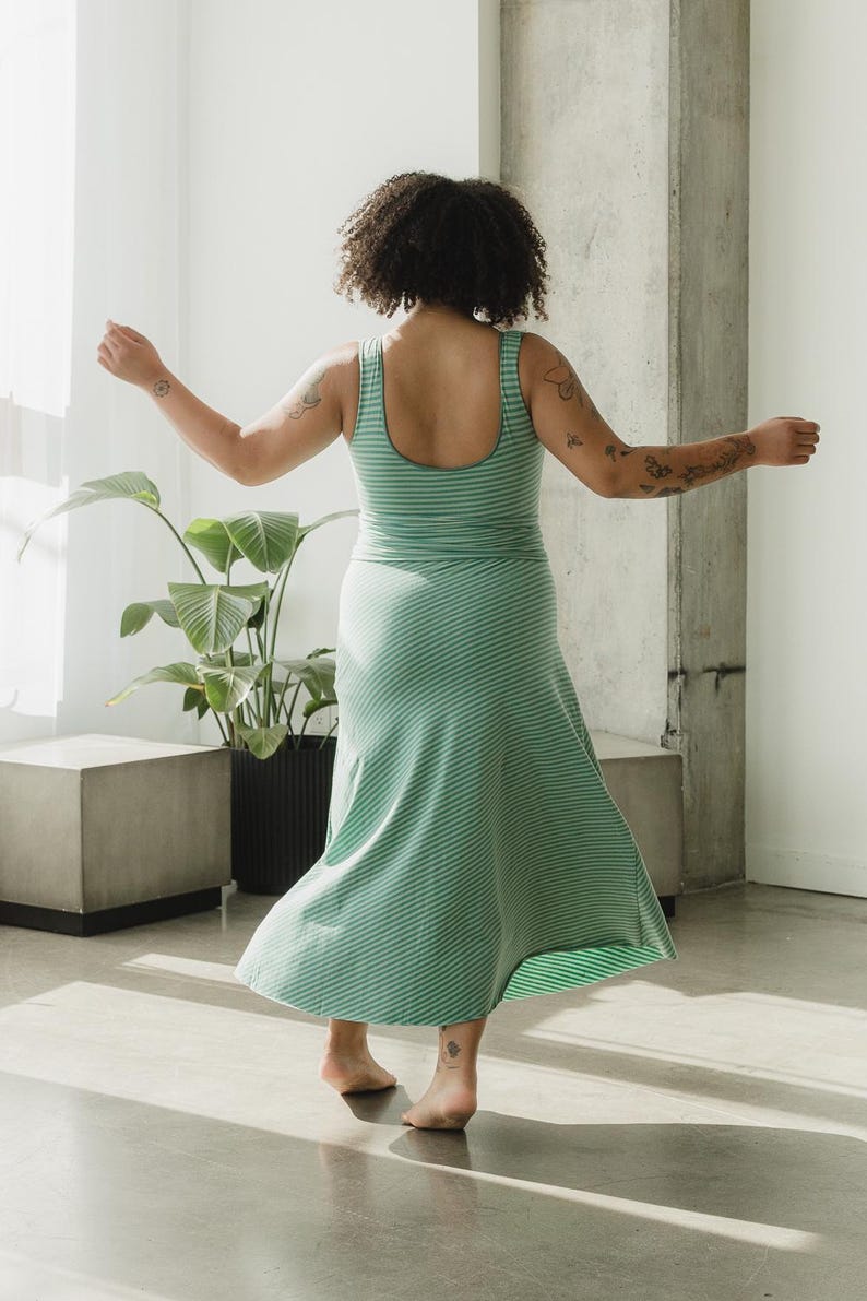 May include: A sleeveless dress featuring a scoop neckline and a flared skirt, crafted from a light green and dark green striped fabric. The garment has a fitted bodice that transitions into a flowing, diagonal-striped skirt that reaches mid-calf.