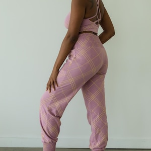 May include: A matching set of lilac-colored activewear. The set includes a sports bra with crisscross straps and high-waisted joggers. Both pieces feature a plaid pattern in a lighter shade of yellow. The joggers have elastic cuffs at the ankles.