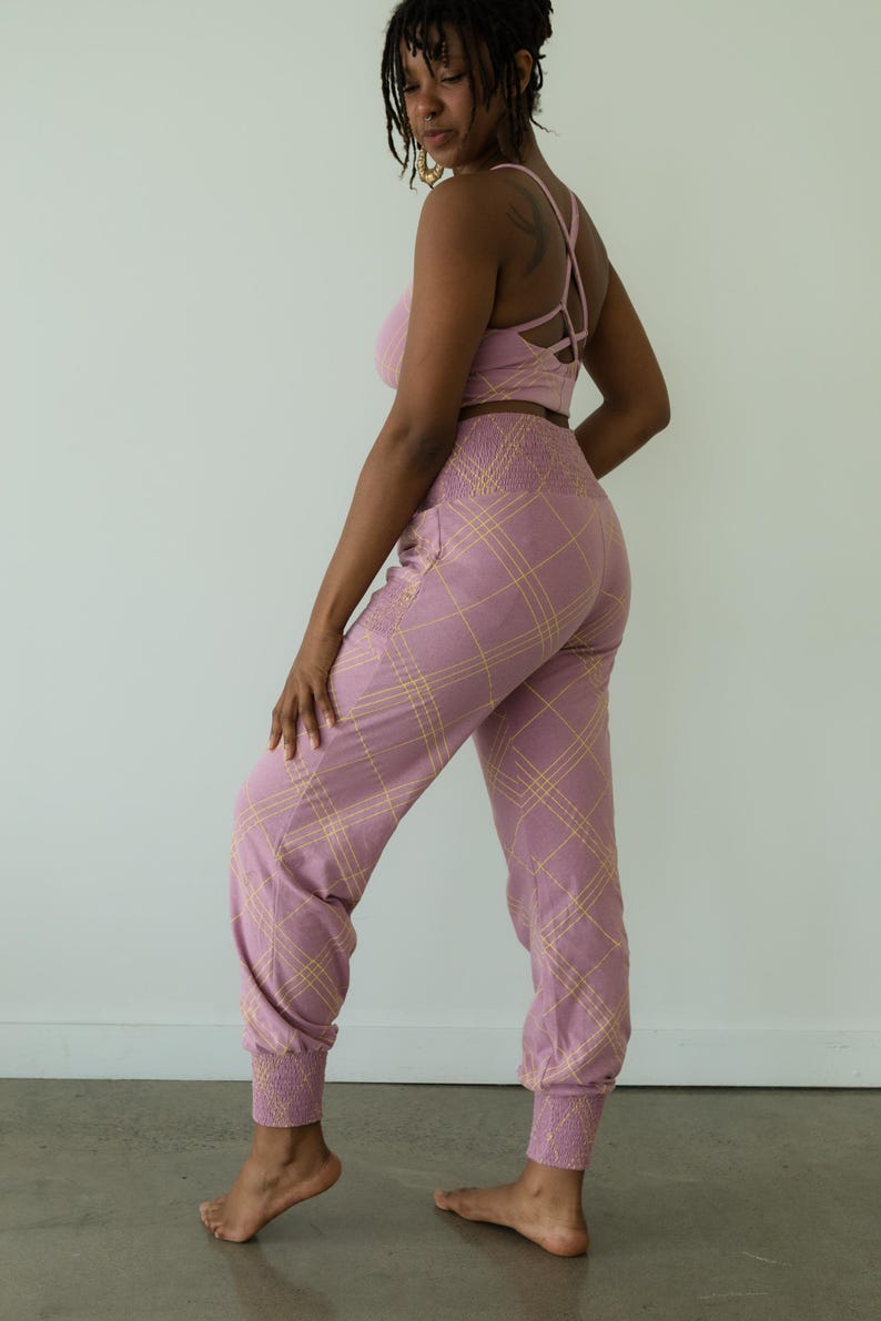 May include: A matching set of lilac-colored activewear. The set includes a sports bra with crisscross straps and high-waisted joggers. Both pieces feature a plaid pattern in a lighter shade of yellow. The joggers have elastic cuffs at the ankles.
