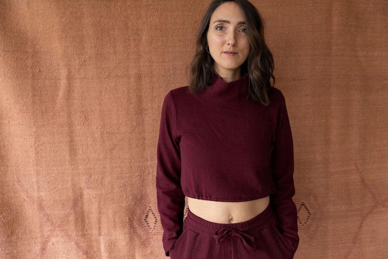 May include: A woman wearing a maroon long-sleeved crop top and matching pants. The top has a mock neck and the pants have a drawstring waist.