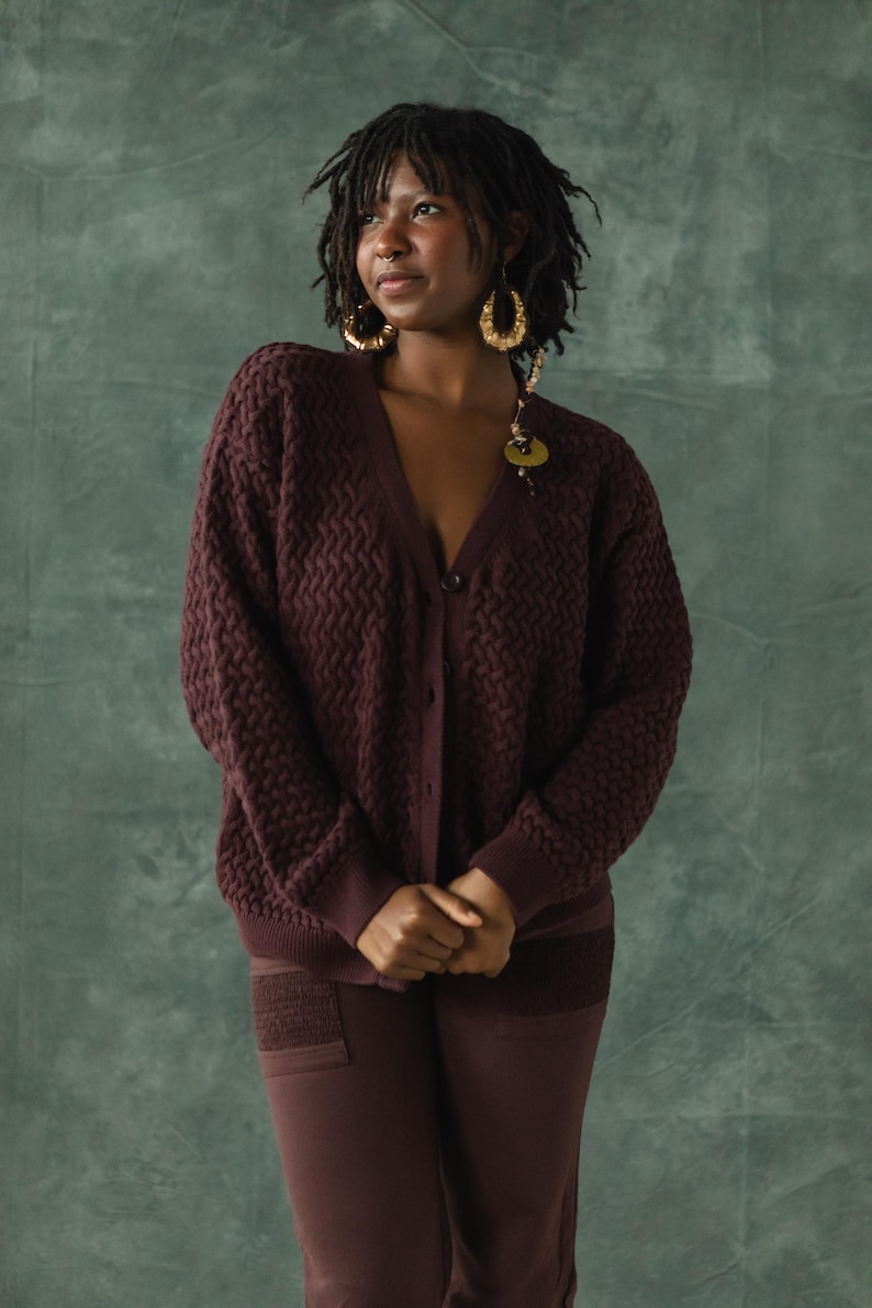 May include: A person wearing a maroon cardigan with a chevron pattern and matching pants. The cardigan has a button closure and the person is wearing gold hoop earrings.