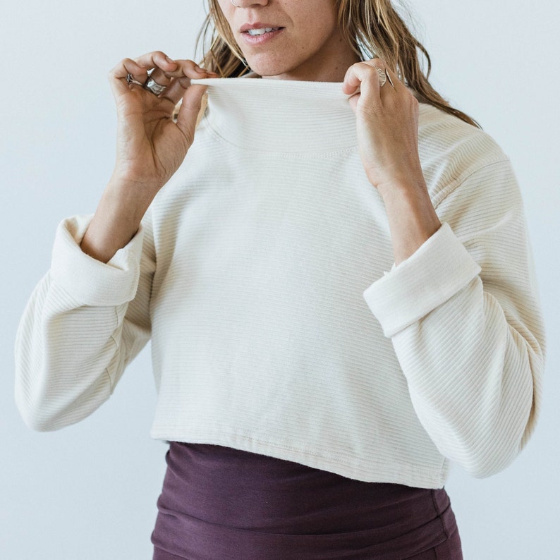 May include: A white cropped sweater with a mock neck and long sleeves. The sweater has a ribbed texture and is made of a soft, comfortable fabric.