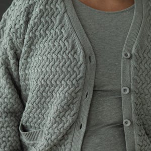 May include: A gray knitted cardigan with a textured pattern and button closure. The cardigan has a relaxed fit and a slightly cropped length.