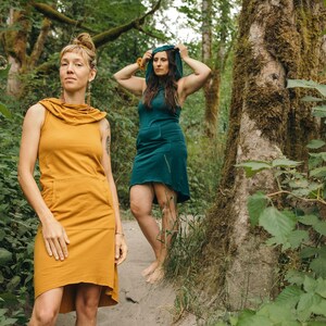 May include: Two people wearing hooded dresses in a forest setting. One dress is mustard yellow and the other is teal.