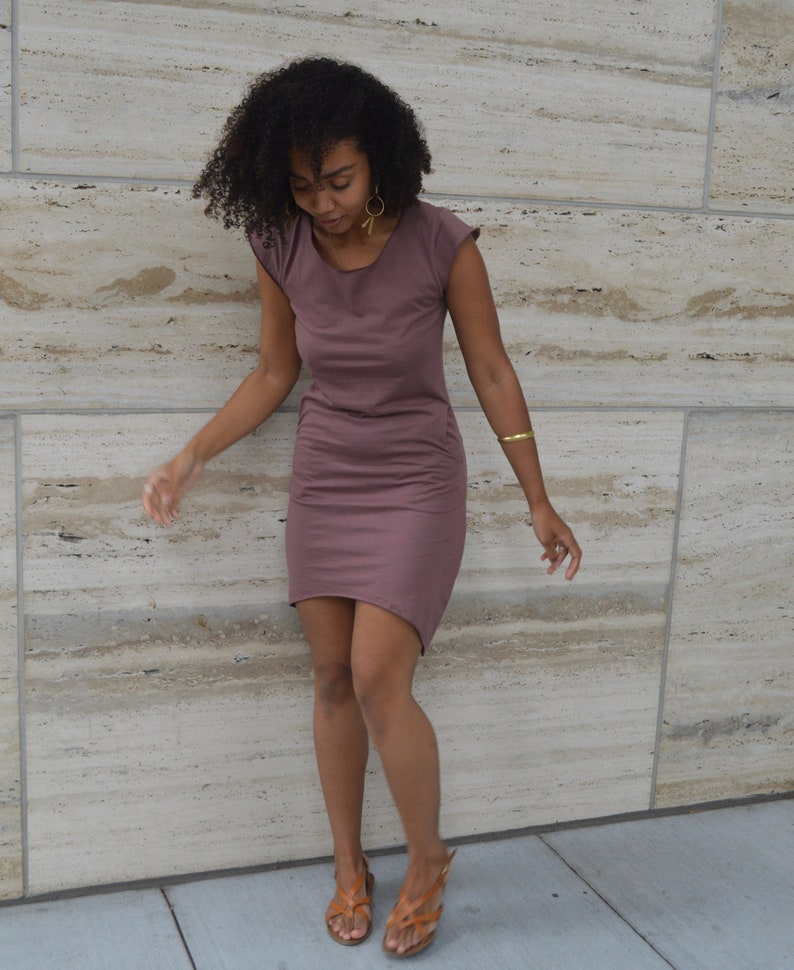 May include: A mauve-colored short-sleeved dress with a round neckline and a high-low hemline. The dress features a simple, solid-colored design with a fitted silhouette that reaches above the knees in the front and slightly longer in the back.