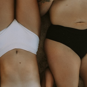 May include: Two people lying on their backs on a sandy beach, wearing white and black underwear.