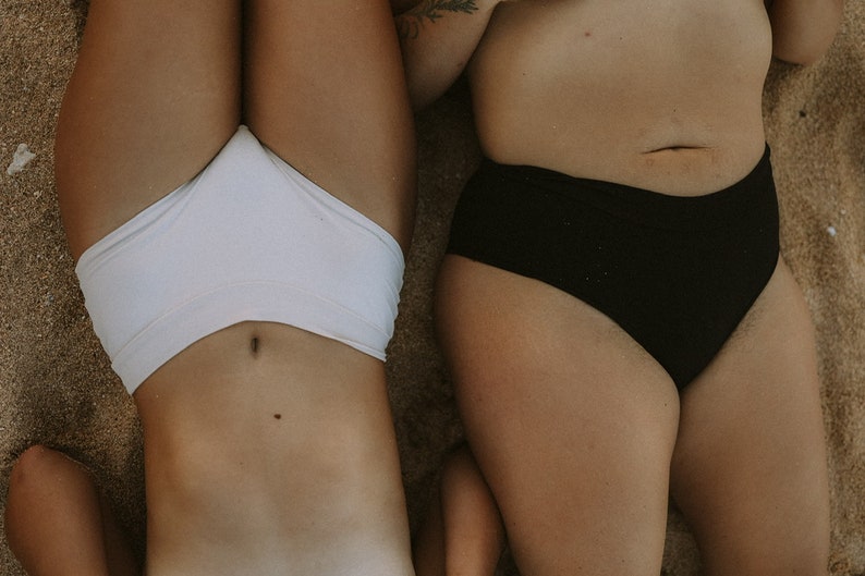 May include: Two people lying on their backs on a sandy beach, wearing white and black underwear.