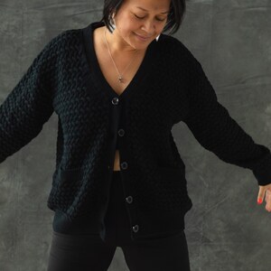 May include: A black knitted cardigan with a v-neck and button closure. The cardigan has a textured pattern and two pockets.