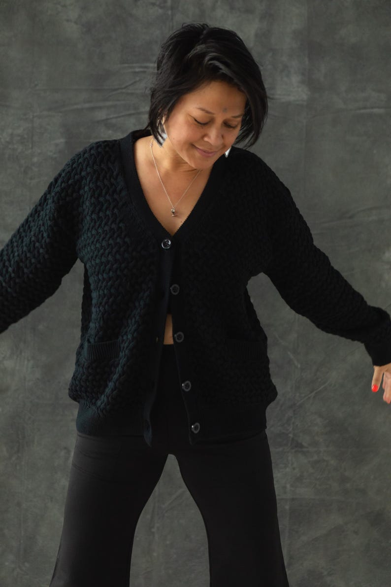 May include: A black knitted cardigan with a v-neck and button closure. The cardigan has a textured pattern and two pockets.