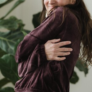 May include: A burgundy velvet sweatshirt with a drawstring waist and elasticated cuffs. The long-sleeved top is a deep, rich colour and has a relaxed fit. The model is wearing black trousers.
