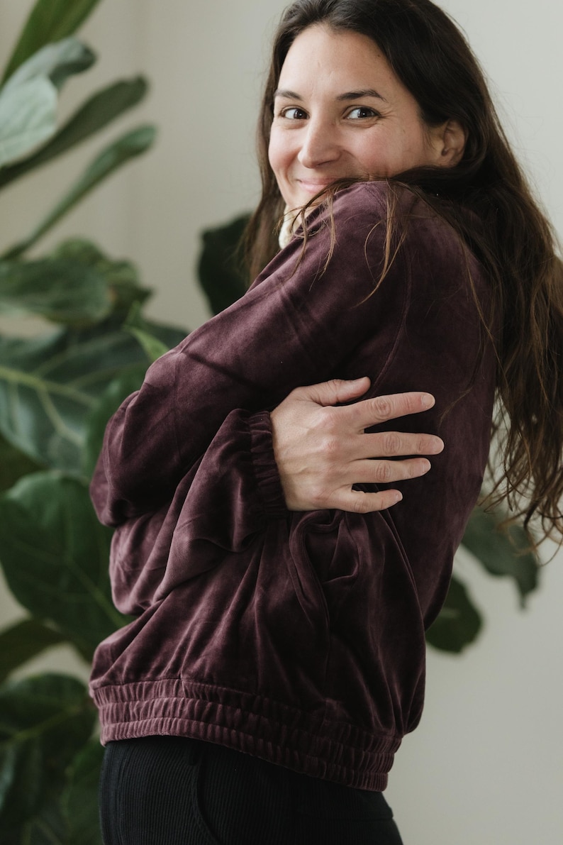 May include: A burgundy velvet sweatshirt with a drawstring waist and elasticated cuffs. The long-sleeved top is a deep, rich colour and has a relaxed fit. The model is wearing black trousers.