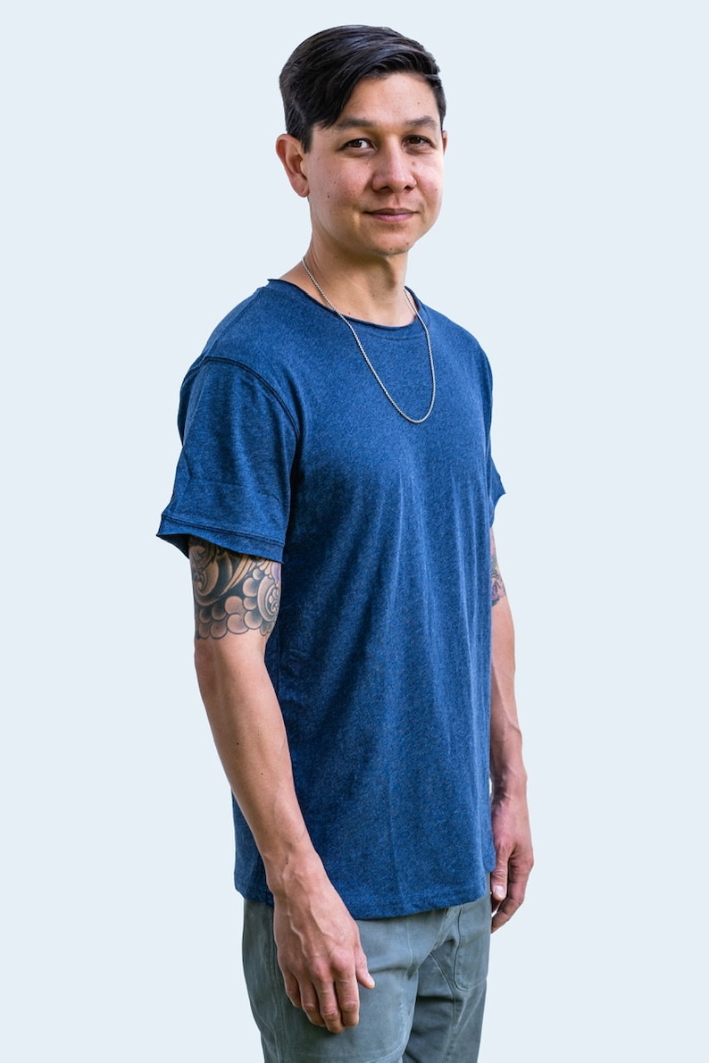 Pu&ograve; includere: Un uomo che indossa una maglietta blu con una collana a catena d'argento. Ha un tatuaggio sul braccio sinistro.