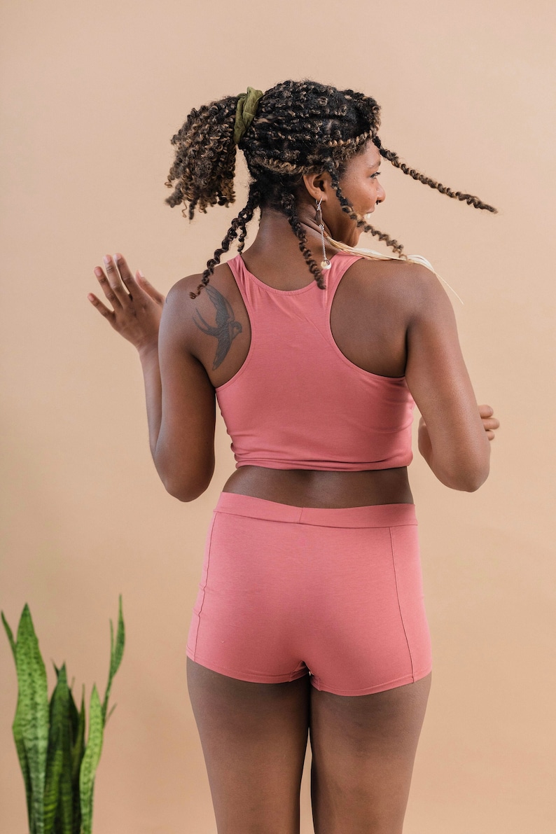 May include: A woman wearing a pink tank top and matching pink shorts. She has a small bird tattoo on her shoulder.