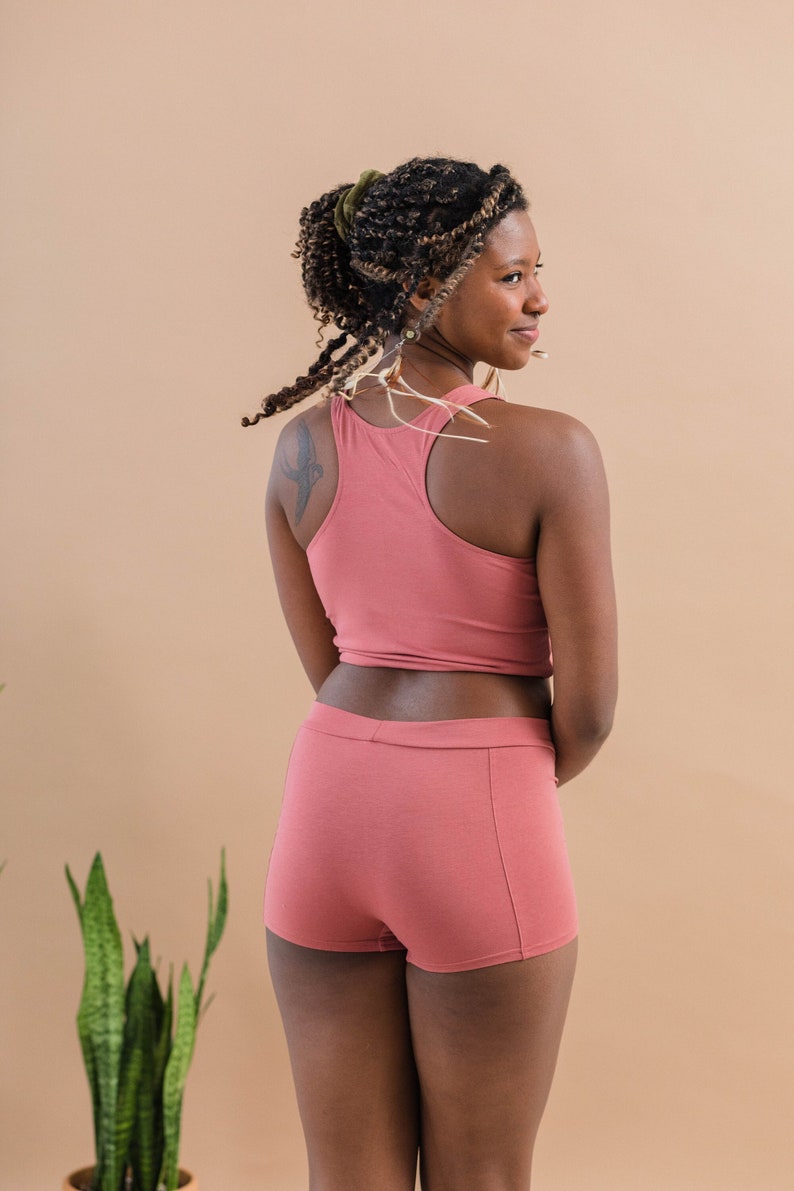 May include: A woman wearing a pink tank top and matching pink shorts. The tank top has a racerback style and the shorts are a boxer style.