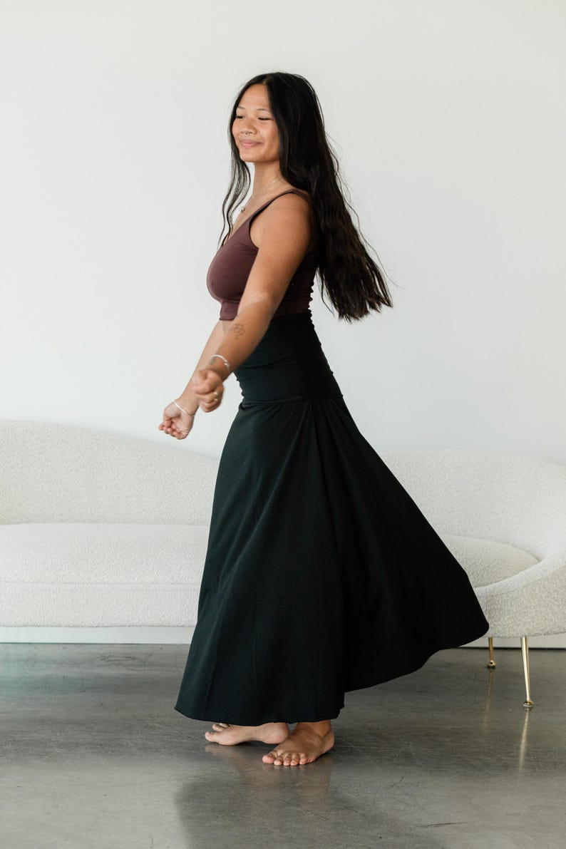 May include: A dark brown sleeveless tank top with a scoop neckline paired with a high-waisted black maxi skirt that features a wide waistband and a flared, flowing silhouette that reaches down to the ankles.