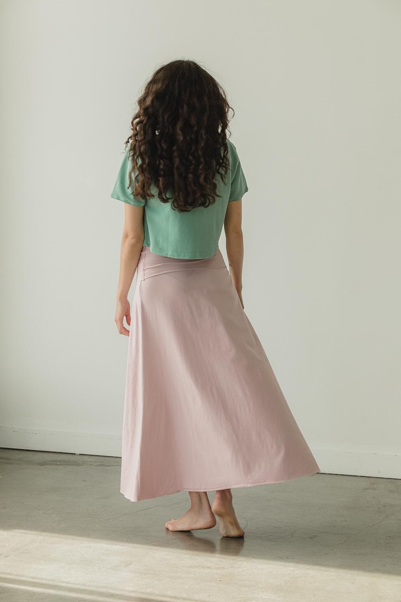 May include: A sage green short-sleeved crop top paired with a light pink ankle-length skirt. The skirt features a wide, flat waistband and a flared, flowing silhouette that reaches down to the ankles, while the top has a simple crew neckline.