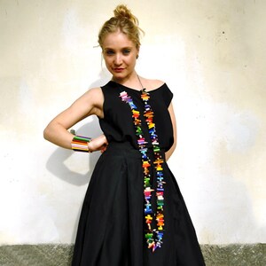 Può includere: Una donna indossa un vestito nero con una lunga collana fatta di matite colorate. La collana è a strati e le arriva fino alla vita.