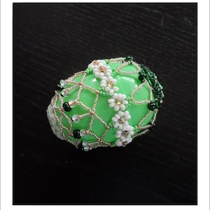 Könnte beinhalten: Ein grünes Osterei, verziert mit weißen und grünen Perlen und einem goldenen und silbernen Drahtgeflecht.