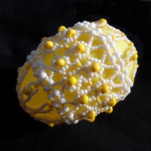 May include: A yellow Easter egg decorated with white and yellow beads in a floral pattern.