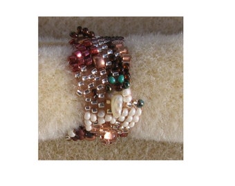 May include: A beaded ring with a multi-colored design featuring brown, white, pink, and green beads. The ring is made with small, square beads and has a unique, textured look.