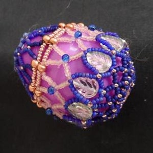 May include: A purple egg-shaped ornament covered in a beaded design with copper, blue, and clear beads.