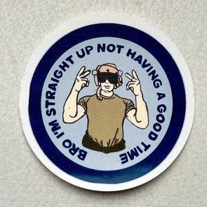 May include: A round sticker with a blue border and a white background. The sticker features a cartoon illustration of a person wearing a helmet and sunglasses, making a peace sign with both hands. The text on the sticker reads "Bro I'm Straight Up Not Having A Good Time".