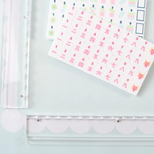 May include: Two sheets of rectangular stickers featuring rows of numbers. One sheet displays Arabic numerals in blue and green, while the other shows pink Chinese characters for numbers one through nine, ending with a small pink dragon icon.