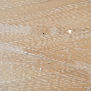 May include: Close-up of a light-colored wooden surface with visible grain and a clear, angled overlay. The overlay appears to be made of a transparent material, possibly acrylic or glass, and is secured with small fasteners.