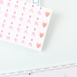 May include: A white sheet of stickers featuring columns of pink Japanese kanji numerals from three to nine. Each row of the number nine is accompanied by a small, pink, cartoon-style dragon head illustration. The stickers are arranged in a grid pattern.