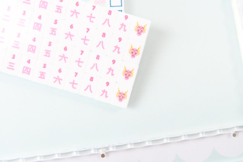 May include: A white sheet of stickers featuring columns of pink Japanese kanji numerals from three to nine. Each row of the number nine is accompanied by a small, pink, cartoon-style dragon head illustration. The stickers are arranged in a grid pattern.