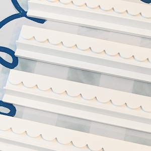 May include: Four white, scalloped-edge wooden shelves are arranged diagonally across a patterned surface. The shelves have a simple, clean design, perfect for displaying items. The background features a blue and white pattern.