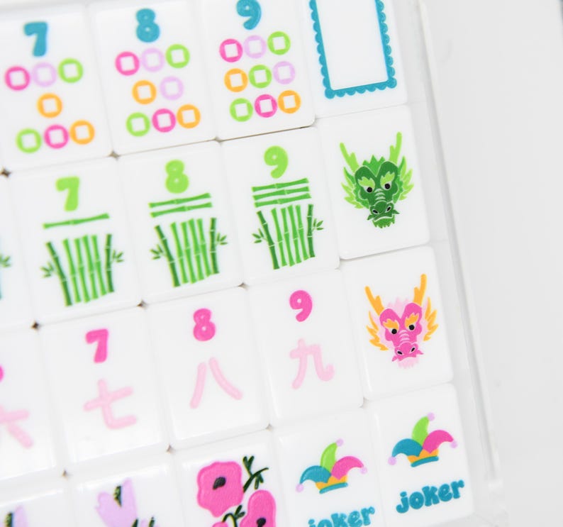 May include: Close-up of white Mahjong tiles with colorful symbols and numbers. Tiles feature green bamboo stalks, pink and orange circles, and dragon illustrations. Some tiles have the word "Joker" printed on them.