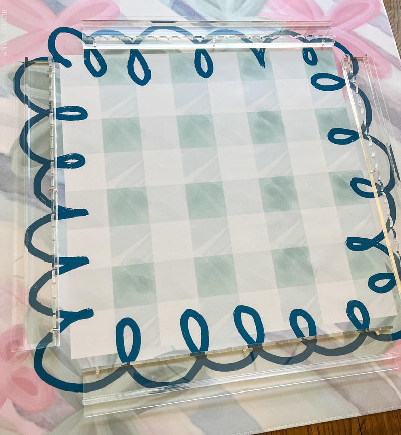 May include: A clear acrylic tray with a scalloped edge design in dark teal. The tray frames a light green and white checkered pattern. The background features a floral and bow design in pink and blue.