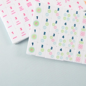 May include: A set of white rectangular mahjong tiles arranged in rows. The tiles feature dark blue Arabic numerals from one to eight, accompanied by circular patterns in green, pink, and blue. Some tiles display pink Chinese characters and a dragon icon.