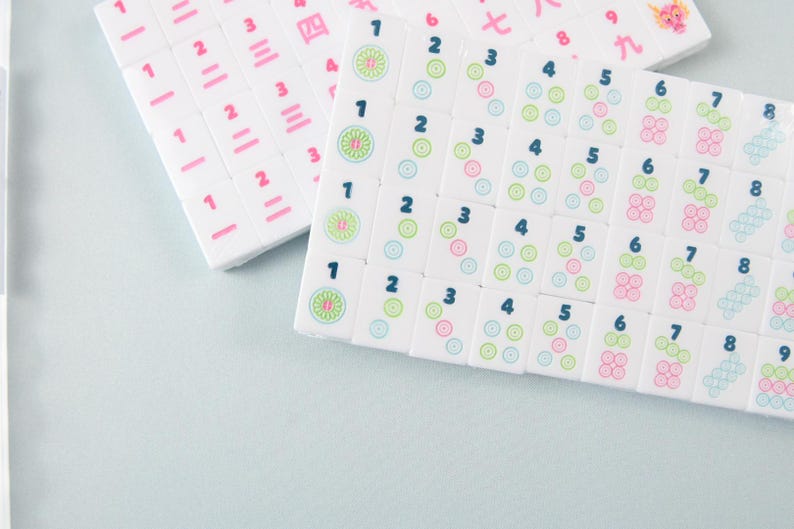 May include: A set of white rectangular mahjong tiles arranged in rows. The tiles feature dark blue Arabic numerals from one to eight, accompanied by circular patterns in green, pink, and blue. Some tiles display pink Chinese characters and a dragon icon.