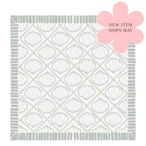 May include: A square textile featuring a repeating diamond grid pattern filled with white seashell illustrations on a light gray background, framed by a border of short vertical gray lines, with a pink flower graphic stating NEW ITEM SHIPS MAY.