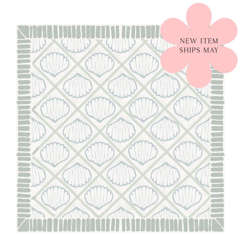 May include: A square textile featuring a repeating diamond grid pattern filled with white seashell illustrations on a light gray background, framed by a border of short vertical gray lines, with a pink flower graphic stating NEW ITEM SHIPS MAY.