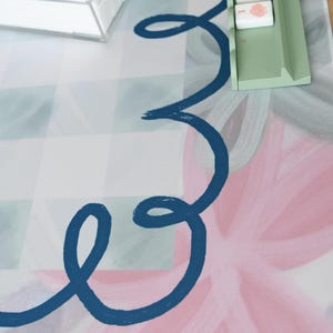 May include: A colorful game mat with a floral design in pink and blue, featuring a navy blue swirl. A clear box and a green tray hold game pieces with illustrations. The background has a checkered pattern.