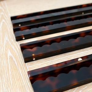 Puede incluir: Tres tiras rectangulares con un patrón de carey en marrón oscuro y negro. Cada tira presenta un borde festoneado en un lado y pequeños detalles metálicos circulares incrustados a intervalos regulares en la superficie plana.