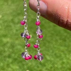May include: Silver dangle earrings with pink and purple gemstones. The earrings feature a delicate chain with multiple small gemstones.