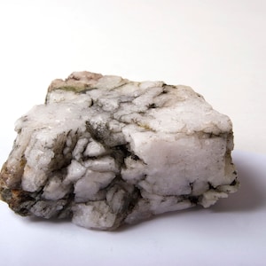 May include: A large, rough, white rock with grey and brown veins and patches. The rock has a jagged, irregular shape.