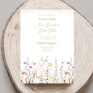 May include: Wedding invitation with a floral border. The invitation is printed on white cardstock with gold lettering. The text reads "Le Invitamos Cordialmente a Nuestra Boda Jeen Beamls & Gloria Estehen SAT 23 SEPT recepcion e seguit La Iglesia Bautista Roman 2310 Calle Doble Ft. Worth, TX 76104"