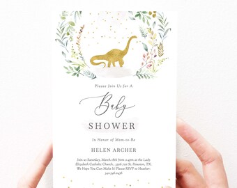 Op de afbeelding: Een witte babyborrel uitnodiging met een gouden dinosaurus silhouet in een groene en bruine bloemenkrans. De tekst luidt: "Kom gezellig mee naar een babyborrel ter ere van de aanstaande moeder HELEN ARCHER. We komen samen op zaterdag 18 maart van 14:00 tot 16:00 uur in de Lady Elizabeth Catholic Church... 3306 71st St. Houston, TX. We hopen dat je erbij kunt zijn! Laat het Heather weten als je komt: 342.546.2456"