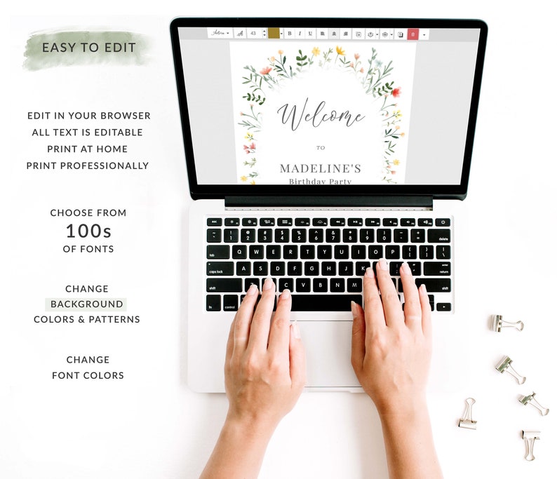 May include: A laptop computer displaying a welcome sign with a floral wreath design. The sign says "Welcome to Madeline's Birthday Party". The laptop is on a white surface with silver paper clips.