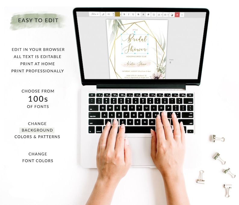 May include: A laptop computer with a screen displaying a customizable bridal shower invitation template. The invitation features a gold geometric frame with green foliage and the text "It's a Bridal Shower" in a gold script font. The text "Honoring Bride-to-Be" is in a smaller font below the main text. The invitation also includes the bride's name, the date, time, and location of the shower. The laptop is on a white surface with paper clips.