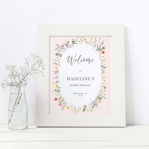 May include: A printable bridal shower welcome sign with a floral wreath design. The sign is on a pink background and says "Welcome to Madeline's Bridal Shower, September 24, 2020".