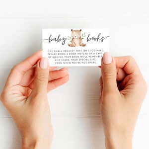 May include: A white card with brown text that reads "baby books". The card features a small illustration of a brown bear with green leaves. The text on the card reads: "One small request that isn't too hard, please bring a book instead of a card. By signing your book we'll remember and share, your special gift, even when you're not there."