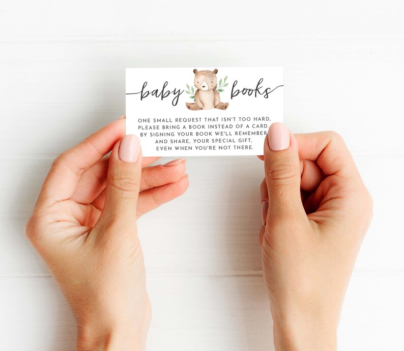 May include: A white card with brown text that reads "baby books". The card features a small illustration of a brown bear with green leaves. The text on the card reads: "One small request that isn't too hard, please bring a book instead of a card. By signing your book we'll remember and share, your special gift, even when you're not there."