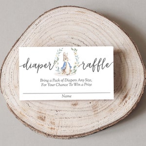 May include: A white card with a watercolor illustration of a rabbit wearing a blue jacket. The card says "diaper raffle" and "Bring a pack of diapers any size, for your chance to win a prize". There is a line for a name at the bottom.