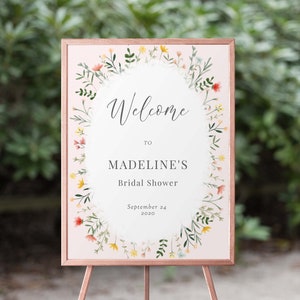 May include: A welcome sign for a bridal shower with a floral wreath border. The sign is on a pink background and says "Welcome to Madeline's Bridal Shower September 24, 2020".